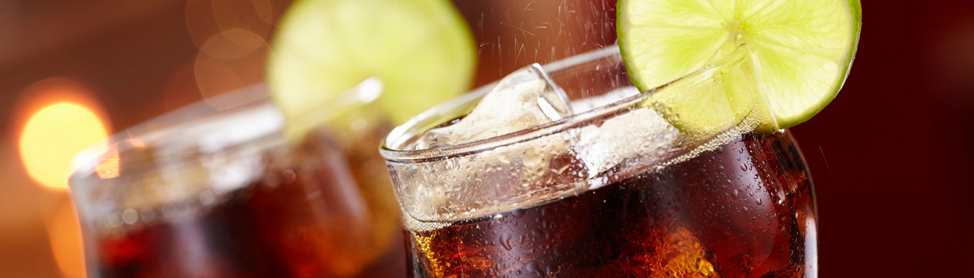 two glasses filled with cola and ice with a wedge of lime
