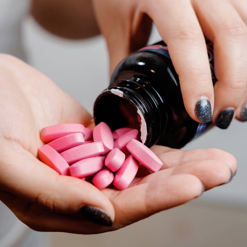 A hand with nail polish pours out pink tablets onto palm